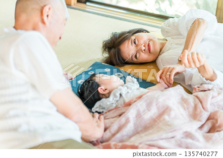 Grandma and Grandpa putting their granddaughter to sleep for a nap on the tatami mat (three-generation family, homecoming, visiting home) Grandma and Grandpa putting their granddaughter to sleep for a nap on the tatami mat (three-generation family, homecoming, visiting home) 135740277