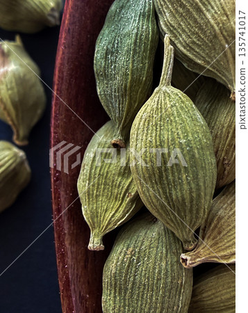 Macro of Green Cardamom Pods in Wooden Spoon on Black Background Macro of Green Cardamom Pods in Wooden Spoon on Black Background 135741017