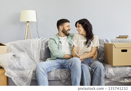 Smiling couple hugging on sofa among boxes after moving into their new home 135741232