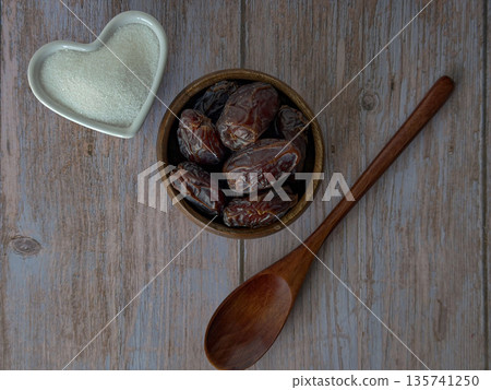 Dried Dates in Wooden Bowl with Spoon and Cane Sugar Heart on Rustic Table 135741250