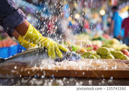 Busy wet market stall scene with person cleaning fresh fish under splashing water, vibrant produce in background, lively atmosphere, yellow gloves, energetic mood 135741592