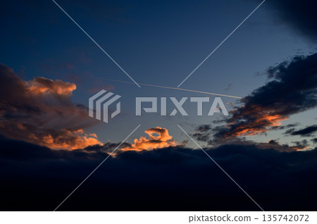夕陽西下,落日餘暉將雲朵染成橘色,一條飛機尾跡筆直地飛過雲層上方。 夕陽西下,落日餘暉將雲朵染成橘色,一條飛機尾跡筆直地飛過雲層上方。 135742072
