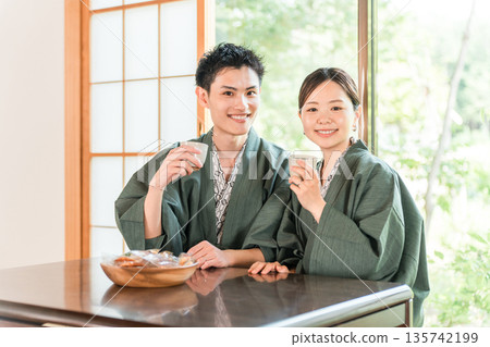 A couple in yukata drinking tea in a Japanese-style room at a ryokan with a garden view A couple in yukata drinking tea in a Japanese-style room at a ryokan with a garden view 135742199