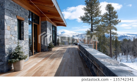 Modern alpine cabin with schist stone wall and wood deck overlooking snowy mountains. 135742341
