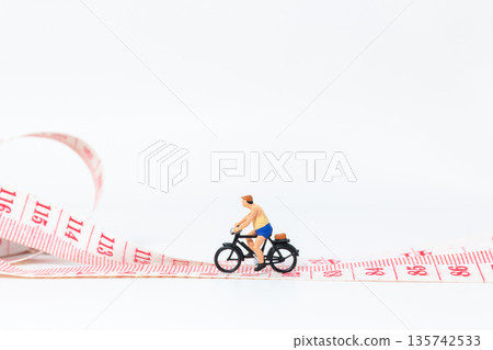 Miniature Cyclist Riding Bicycle on Measuring Tape 135742533