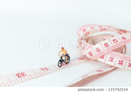 Miniature Cyclist Riding Bicycle on Measuring Tape 135742534