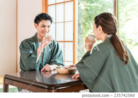 A couple in yukata drinking tea in a Japanese-style room at a ryokan with a garden view A couple in yukata drinking tea in a Japanese-style room at a ryokan with a garden view 135742560