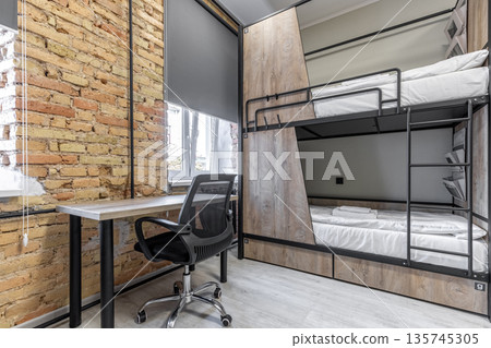 Modern hostel room with industrial bunk beds, desk, and brick wall 135745305