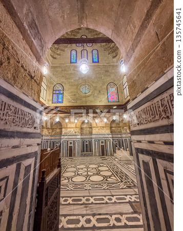 Interior view of Sultan Al-Ashraf Qaytbay Mosque and mausoleum. Features intricate arches, striped wall, and decorative dome. Soft light filters through stained glass window 135745641