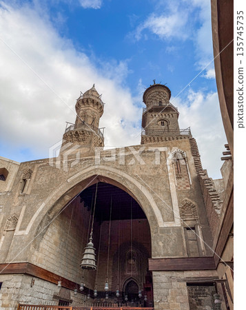 Qalawun complex interior at Al-Muizz Street in Cairo. Features Islamic architecture with arches, intricate designs, and a central courtyard with greenery. Qalawun complex interior at Al-Muizz Street in Cairo. Features Islamic architecture with arches, intricate designs, and a central courtyard with greenery. 135745735