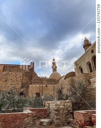 Qalawun complex interior at Al-Muizz Street in Cairo. Features Islamic architecture with arches, intricate designs, and a central courtyard with greenery. Qalawun complex interior at Al-Muizz Street in Cairo. Features Islamic architecture with arches, intricate designs, and a central courtyard with greenery. 135745739