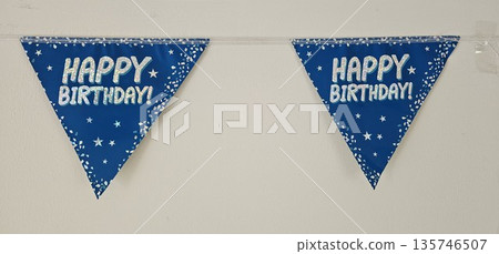 A blue banner with stars and the words Happy Birthday! is hanging on a wall 135746507
