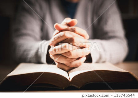 Clasped hands in prayer over an open book, warm light and shallow depth of field, symbolizing faith, devotion, reflection and hope for spiritual guidance during quiet study at home. Clasped hands in prayer over an open book, warm light and shallow depth of field, symbolizing faith, devotion, reflection and hope for spiritual guidance during quiet study at home. 135746544