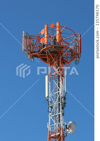 The upper portion of a telecommunications tower rising against a clear, cloudless blue sky. 135746570