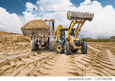 Construction activity is taking place as heavy machinery moves sand, creating deep tracks on the sandy surface under a cloudy sky Construction activity is taking place as heavy machinery moves sand, creating deep tracks on the sandy surface under a cloudy sky 135746590