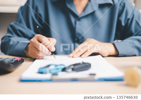 Person signing auto loan agreement on clipboard with car keys and calculator on desk, completing vehicle purchase paperwork, financing approval, insurance details and budget planning. Person signing auto loan agreement on clipboard with car keys and calculator on desk, completing vehicle purchase paperwork, financing approval, insurance details and budget planning. 135746630