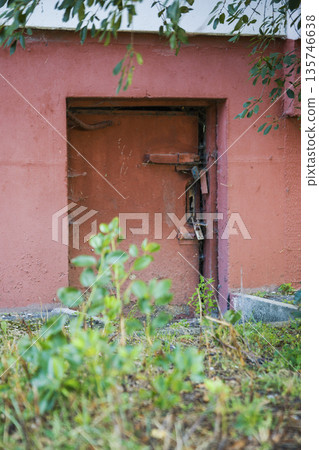 A door built into a wall is locked and surrounded by overgrown plants near an old building on a sunny day in an unvisited part of the city A door built into a wall is locked and surrounded by overgrown plants near an old building on a sunny day in an unvisited part of the city 135746638