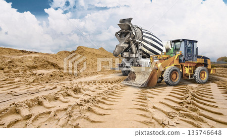 Heavy machinery leaves deep tracks in sandy ground as a loader works near a large pile of sand under a cloudy sky signaling ongoing construction activity Heavy machinery leaves deep tracks in sandy ground as a loader works near a large pile of sand under a cloudy sky signaling ongoing construction activity 135746648
