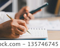 Close-up of hands writing notes in a notebook while holding a smartphone, organizing tasks, budgeting and tracking expenses for business productivity, planning and remote work communication. 135746745