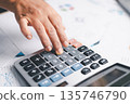 Close-up hand using calculator on office desk with financial charts and reports, budgeting and accounting for business analysis, tax planning, audit and expense control in workplace finance. 135746790