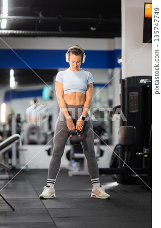 Woman exercising with kettlebell in modern gym Woman exercising with kettlebell in modern gym 135747749
