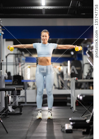 Woman exercising with dumbbells doing lateral raise 135747758