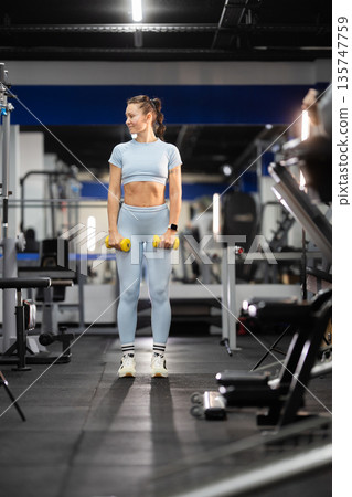 Woman exercising with dumbbells in modern gym Woman exercising with dumbbells in modern gym 135747759