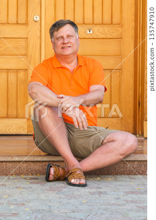 A man in casual clothes sits on the porch of his house 135747910