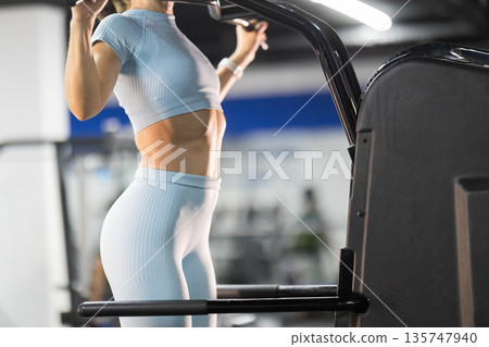 Fit woman training pull-ups on gym equipment 135747940
