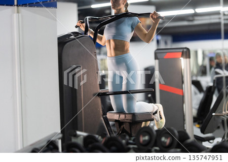 Woman performing knee raises on assisted dip machine in gym 135747951
