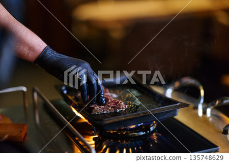 Chef Hands Cook Steak On Grill Pan Over Open Flame In Modern Kitchen Studio Setup Chef Hands Cook Steak On Grill Pan Over Open Flame In Modern Kitchen Studio Setup 135748629