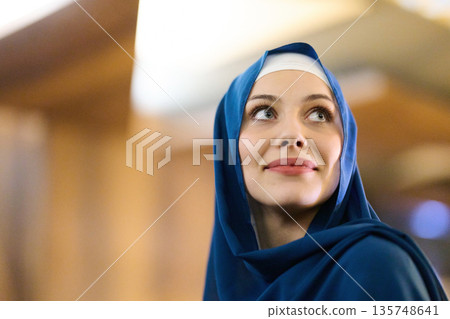 Portrait Of A Woman In Blue Hijab Looking Up With A Gentle Smile 135748641
