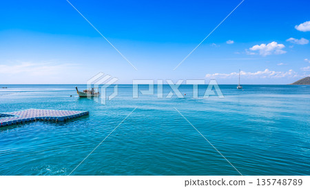 Serene view of traditional and modern boats floating on calm turquoise waters near Koh Samed island under a bright blue sky Serene view of traditional and modern boats floating on calm turquoise waters near Koh Samed island under a bright blue sky 135748789