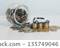 Spilled coin jar with stacks of coins and a miniature silver car on white background, symbolizing saving for a vehicle, down payment goals, auto loan budgeting and financial planning. 135749046