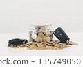 Car key fob and toy car beside a coin jar and scattered change on white background, symbolizing saving for a vehicle, down payment budgeting, auto loan planning and smart finance goals. 135749050