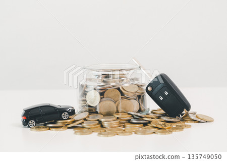 Car key fob and toy car beside a coin jar and scattered change on white background, symbolizing saving for a vehicle, down payment budgeting, auto loan planning and smart finance goals. 135749050