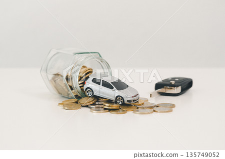 Spilled coin jar with miniature silver car and key fob on white background, symbolizing saving for a vehicle, down payment goals, auto loan budgeting and smart finance purchase planning. Spilled coin jar with miniature silver car and key fob on white background, symbolizing saving for a vehicle, down payment goals, auto loan budgeting and smart finance purchase planning. 135749052