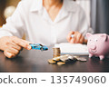 Hand holding a toy car beside stacked coins and a pink piggy bank on desk, symbolizing car savings, down payment budgeting, auto loan planning and smart personal finance goals for car purchase. 135749060