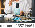 Hand holding car key above blue piggy bank beside coin jar, cash and calculator, showing car savings, auto loan planning, down payment budgeting and personal finance goals. 135749061