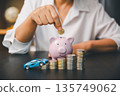 Hand putting coin into pink piggy bank beside toy car and stacked coins, showing car savings, down payment goals, auto loan budgeting and smart personal finance planning for vehicle purchase. 135749062