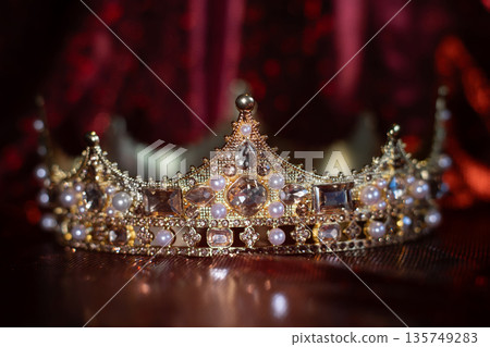 Ancient golden medieval crown with gemstones on sparkle red background. 135749283