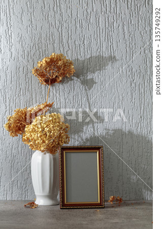 Empty picture frame and white vase with dry flowers on a background of gray wall. Empty picture frame and white vase with dry flowers on a background of gray wall. 135749292
