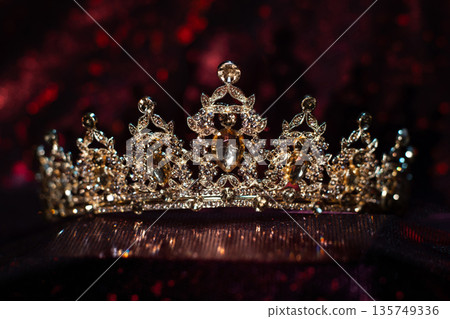 Golden yellow crown with citrines, gemstones on dark sparkle red background. Golden yellow crown with citrines, gemstones on dark sparkle red background. 135749336