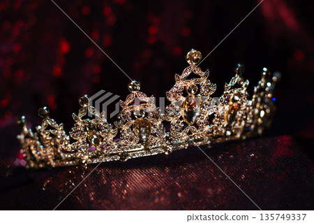 Golden yellow crown with citrines, gemstones on dark sparkle red background. 135749337