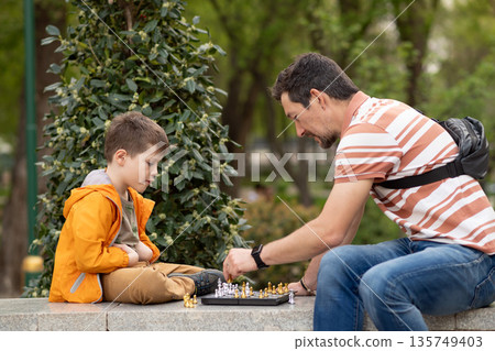 Boy with father playing chess outdoor. Learning strategic game. Education. Boy with father playing chess outdoor. Learning strategic game. Education. 135749403