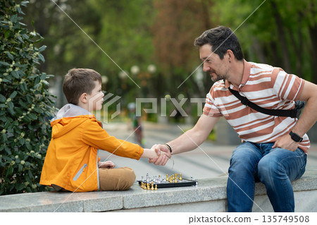 Boy with father playing chess outdoor. Handshake, clasp, handclasp. Boy with father playing chess outdoor. Handshake, clasp, handclasp. 135749508