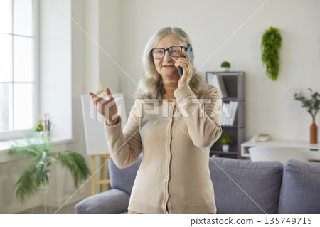 Happy senior woman talking on mobile phone with gestures and smiling at home Happy senior woman talking on mobile phone with gestures and smiling at home 135749715