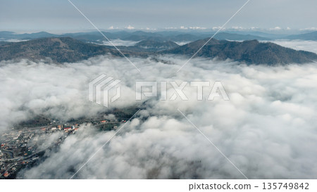 Above the clouds. Foggy layered mountain landscape with a city in Carpathians, Ukraine. 135749842