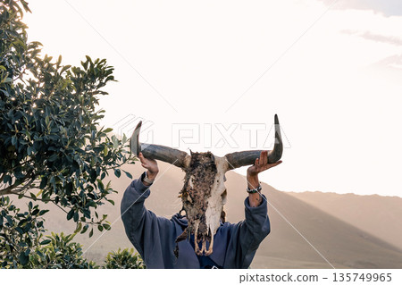 Wildebeest skull with large horns in hands. Spiritual ritual or nature connection concept. animal mask Wildebeest skull with large horns in hands. Spiritual ritual or nature connection concept. animal mask 135749965