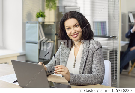 Smiling businesswoman working on financial planning at laptop in bright office 135750229